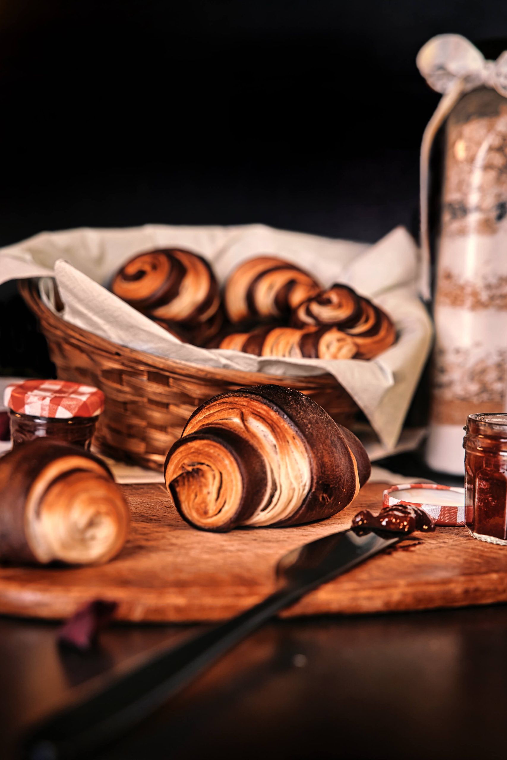 Schokoladen Croissants mit Erdbeermarmelade mit einem Messer auf einen Holzbrett vor einem Brotkorb